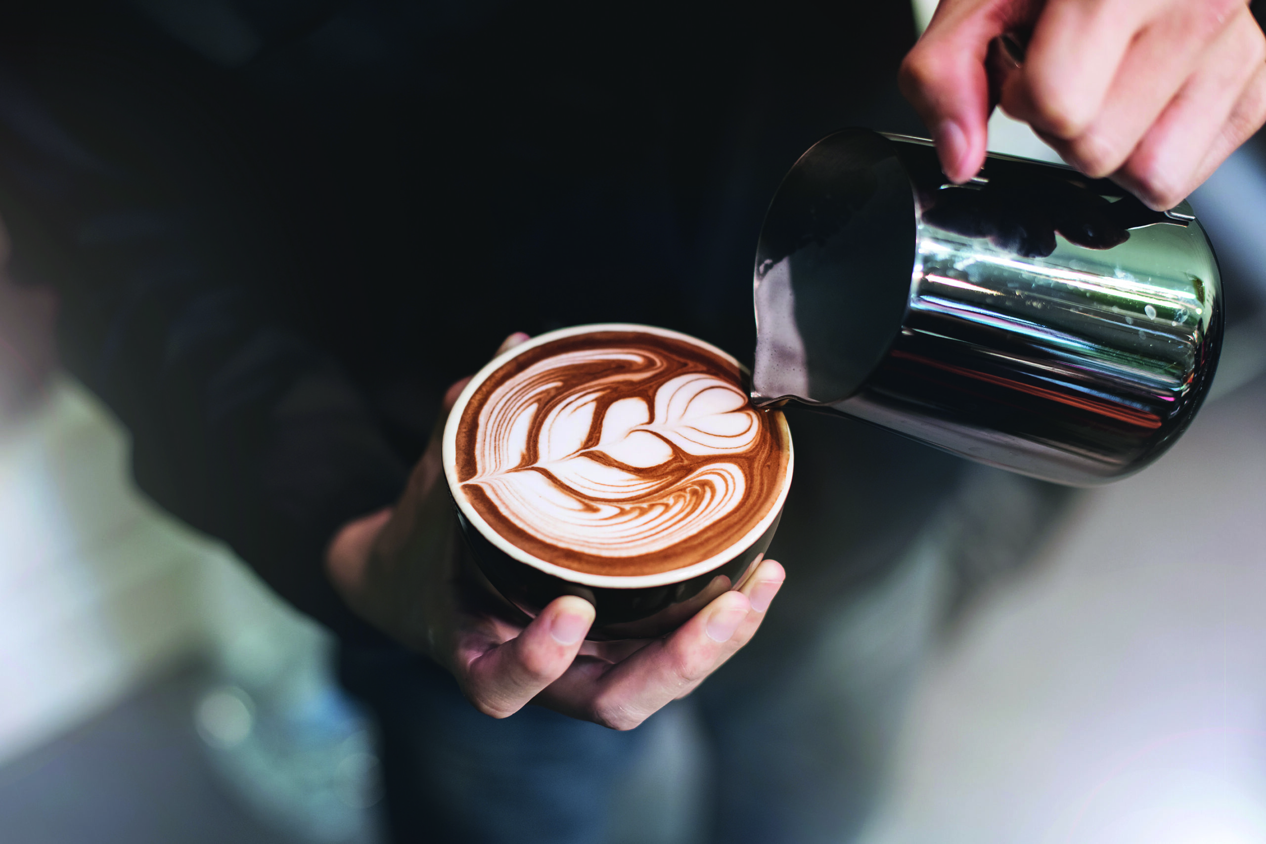 cappuccino mit Herzchen barista hand giesst gerade milch ein