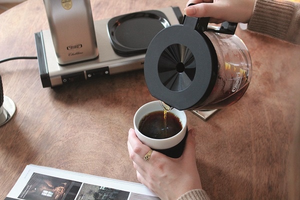Frauenhand giesst Kaffee aus Glaskanne in eine Tasse