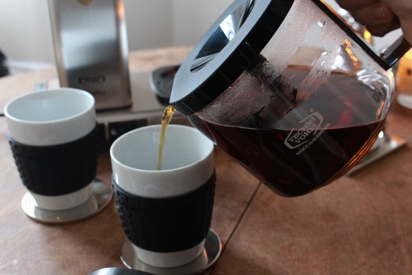Glaskanne mit Trichter giesst Kaffee in Becher