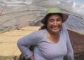 lachende Frau mit Hut vor Stellagen im Hintergrund mit Kaffeebohnen