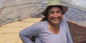 lachende Frau mit Hut vor Stellagen im Hintergrund mit Kaffeebohnen