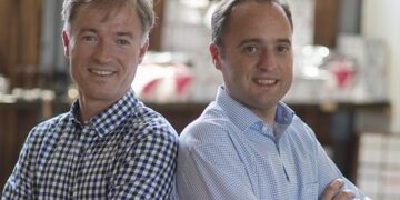 zwie lachende Maenner Ruecken an Ruecken Kaffee wissen