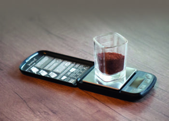 viereckiges Glas mit Kaffeepulver steht auf ausgeklappter Waage für Berechnung von Brew Ratio