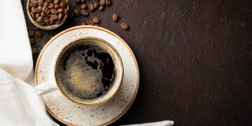 Close-up of a Cup of black coffee and coffee beans on a dark background. Top view with copy space