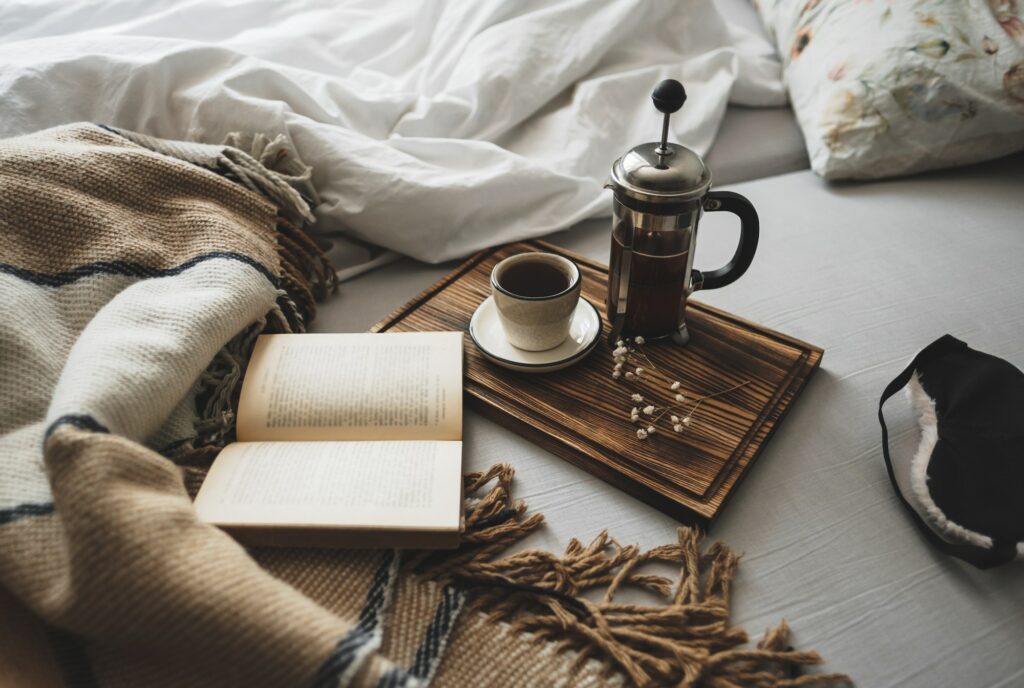 Coffee brewed in a French press and a cup on a wooden board with open book in bed.