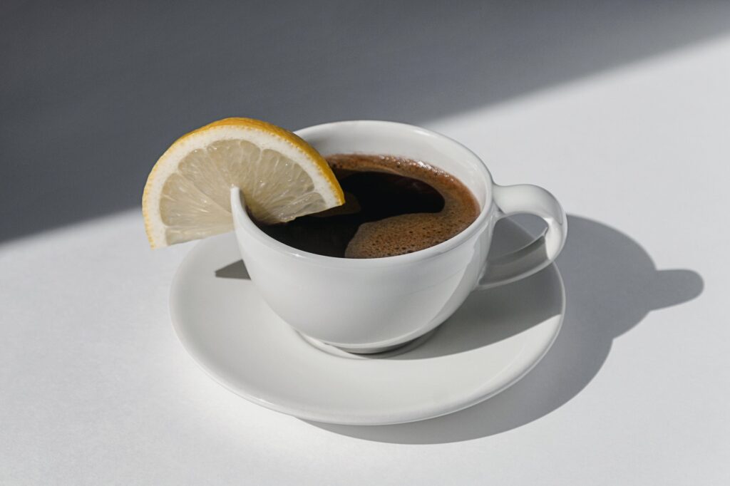 Coffee cup with espresso served with lemon on white background with shadows and sunlight
