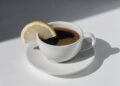 Coffee cup with espresso served with lemon on white background with shadows and sunlight