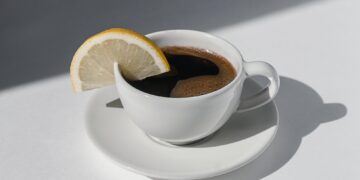 Coffee cup with espresso served with lemon on white background with shadows and sunlight