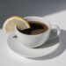 Coffee cup with espresso served with lemon on white background with shadows and sunlight