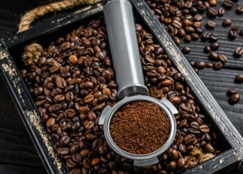 Ground Coffee in Portafilter for Espresso in a wooden tray with coffee beans.