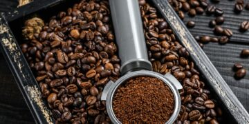 Ground Coffee in Portafilter for Espresso in a wooden tray with coffee beans.