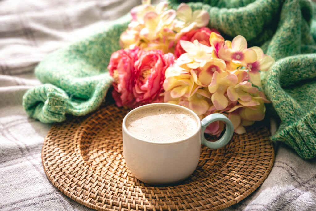 Home composition with a cup of coffee, flowers and a knitted element.