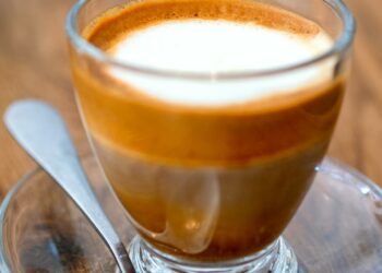 Macchiato coffee drink with foam and layers in glass cup with a spoon on wooden background. Macro cr