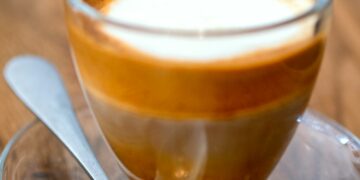 Macchiato coffee drink with foam and layers in glass cup with a spoon on wooden background. Macro cr