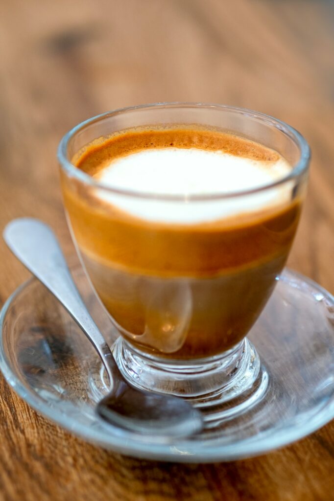 Macchiato coffee drink with foam and layers in glass cup with a spoon on wooden background. Macro cr