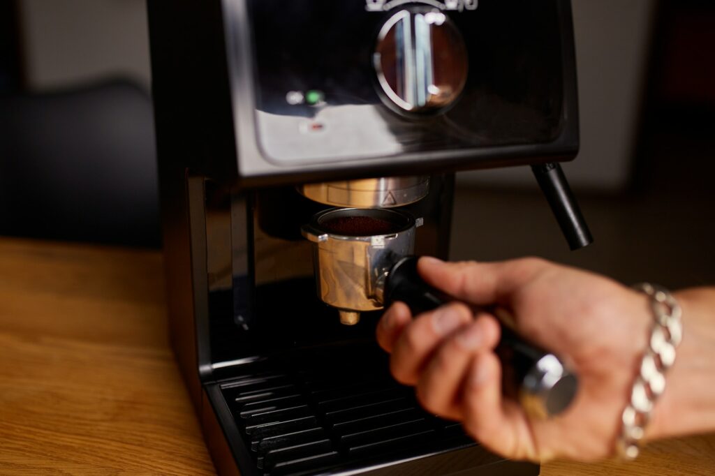 Male barista hand making espresso from ground coffee maker at modern cafe