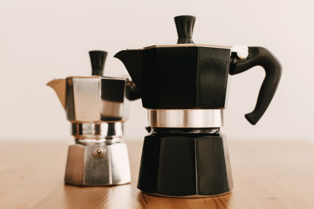 Steel and black geyser coffee makers on wooden table