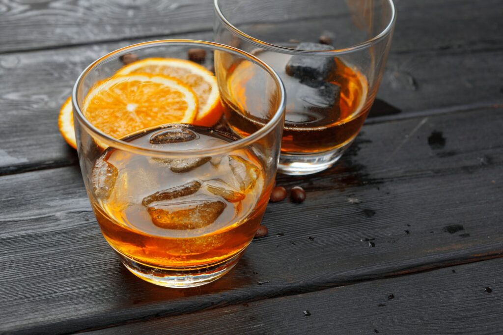Whiskey or liqueur, coffee beans and orange cut on wooden background. Seasonal holidays concept