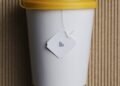 White takeaway paper recycle cup with yellow lid on brown corrugated background.