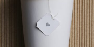 White takeaway paper recycle cup with yellow lid on brown corrugated background.