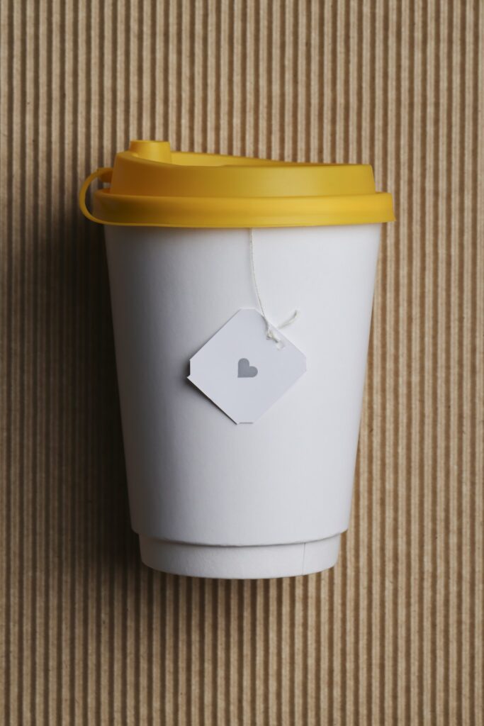 White takeaway paper recycle cup with yellow lid on brown corrugated background.
