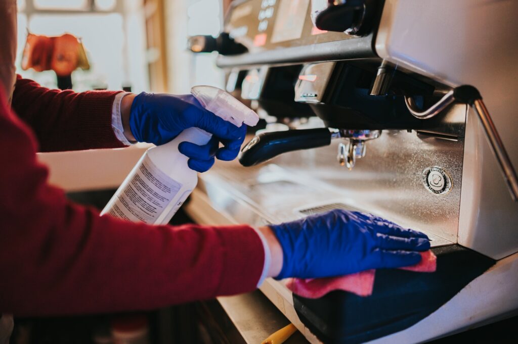 Woman cleaning the coffee machine with sanitizer and towel with blue gloves put on