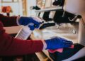 Woman cleaning the coffee machine with sanitizer and towel with blue gloves put on