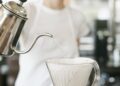 Woman wearing a white apron standing in a coffee shop, making filter coffee.