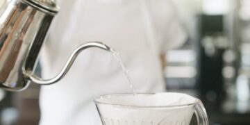 Woman wearing a white apron standing in a coffee shop, making filter coffee.