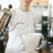 Woman wearing a white apron standing in a coffee shop, making filter coffee.