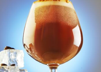 A cold drink or Nitro Coffee drink in a glass with bubble foam and ice on a wooden stand, hero view