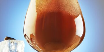 A cold drink or Nitro Coffee drink in a glass with bubble foam and ice on a wooden stand, hero view