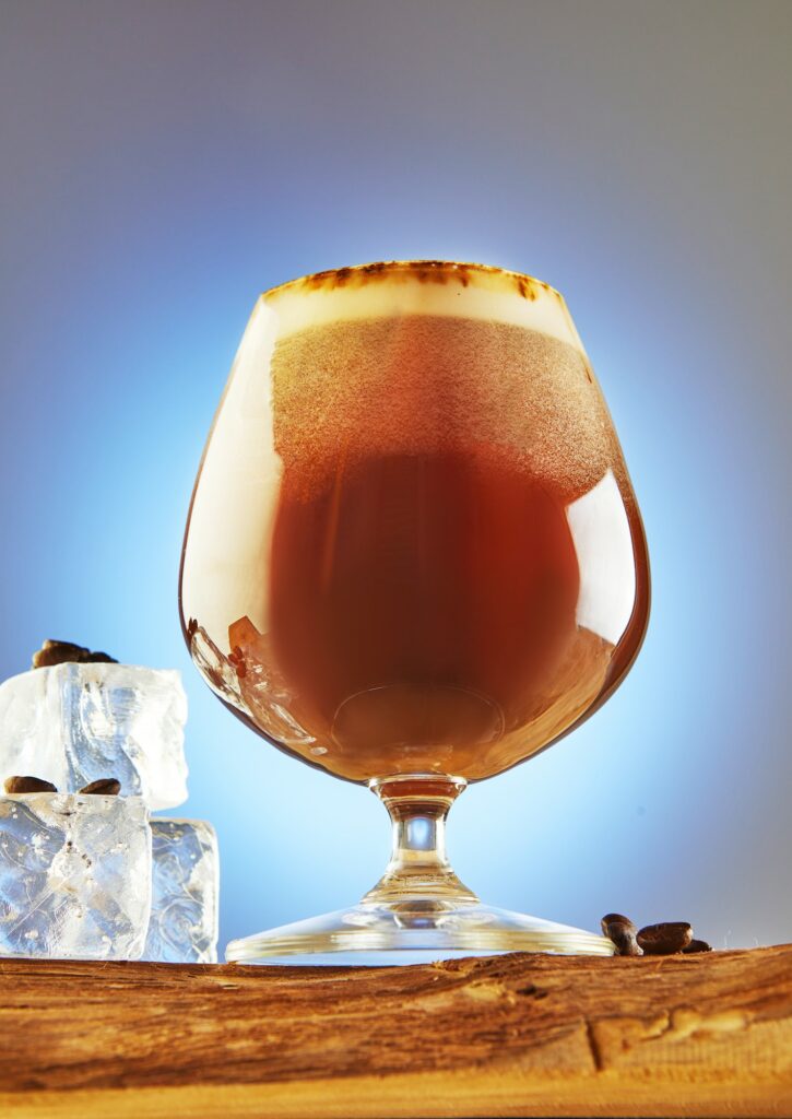 A cold drink or Nitro Coffee drink in a glass with bubble foam and ice on a wooden stand, hero view