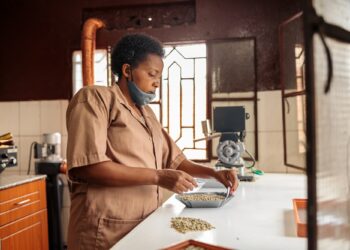 African American woman in face mask stacking coffee beans in a bowl