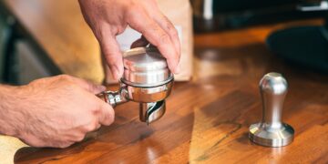 Barista tampering grinded coffee beans to prepare espresso.
