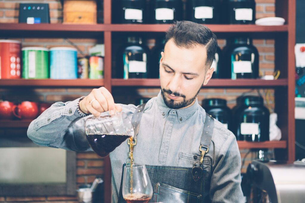 Bearded barista pouring coffee in glass