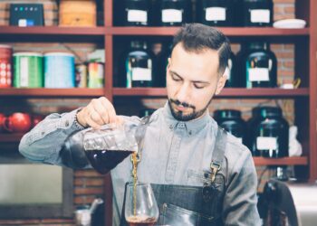 Bearded barista pouring coffee in glass