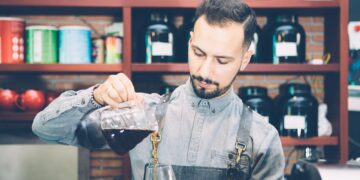 Bearded barista pouring coffee in glass