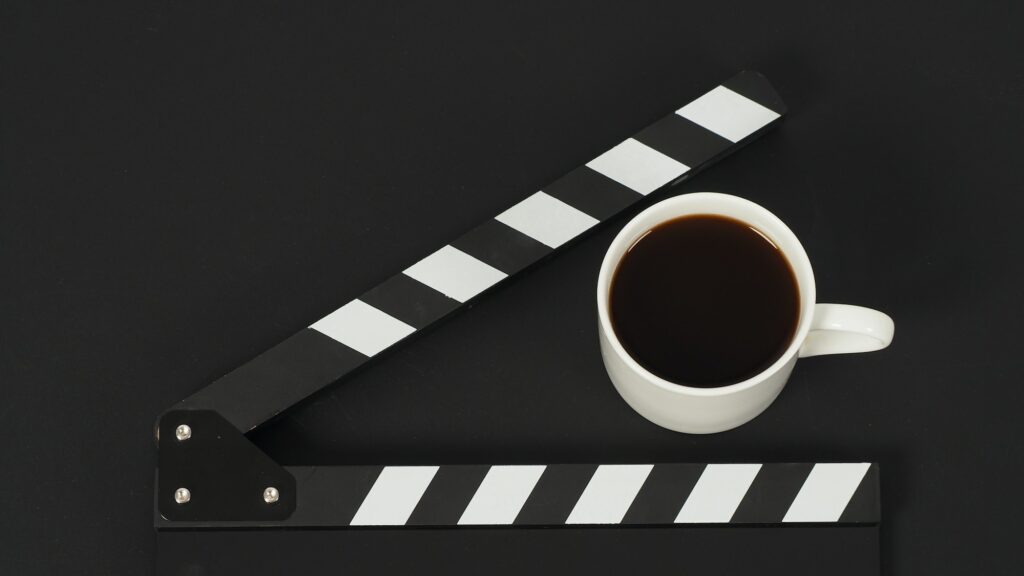 Black clapperboard or movie slate and cup of coffee on black background