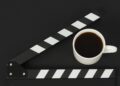 Black clapperboard or movie slate and cup of coffee on black background