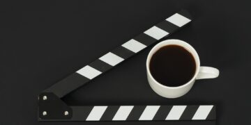 Black clapperboard or movie slate and cup of coffee on black background