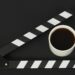 Black clapperboard or movie slate and cup of coffee on black background
