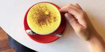Hand holding a cup with a Tumeric latte