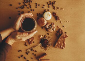 Hands holding glass cup with fresh coffee and roasted beans