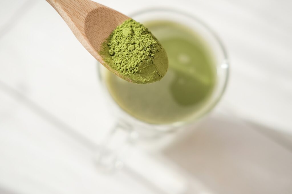 matcha latte in a glass mug and matcha powder in wooden spoon.