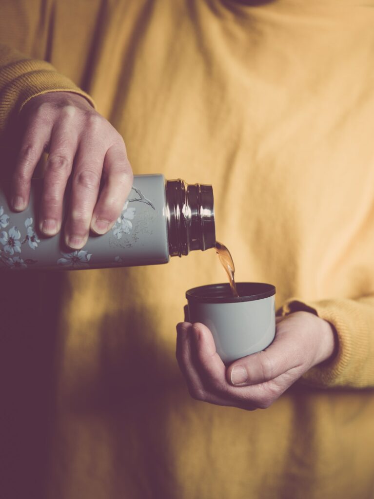 mid section close up of a woman wearing yellow pouring a cup of coffee from a vintage thermos flask