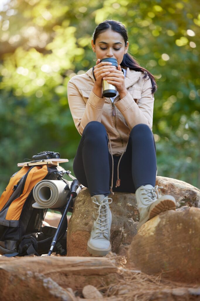 Sports, hiking and woman with coffee in forest to relax from walking, trekking and exercise in morn