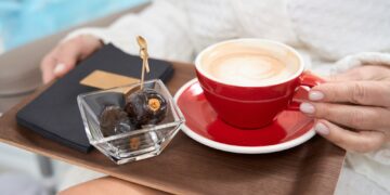 Woman in bathrobe sits with cup of coffee and fruits