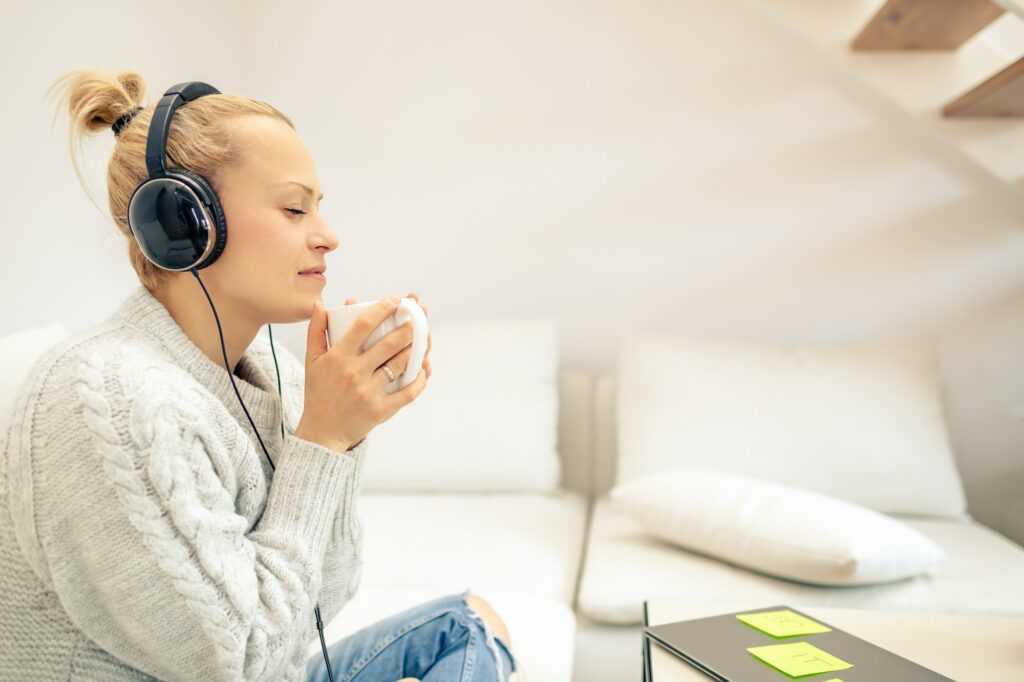 Young woman listening to music and enjoying cup of coffee