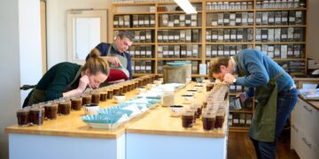 drei Leute ueber Kaffeetassen auf tisch gebeugt und riechen daran